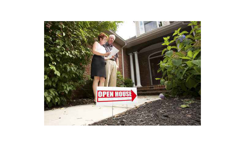 Real estate agent shows a board to a homebuyer next to an open house sign