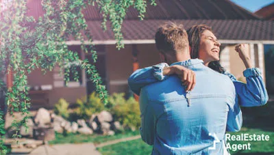 YOUNG COUPLE HUGGING IN FRONT OF A HOME WITH THE KEYS IN HAND